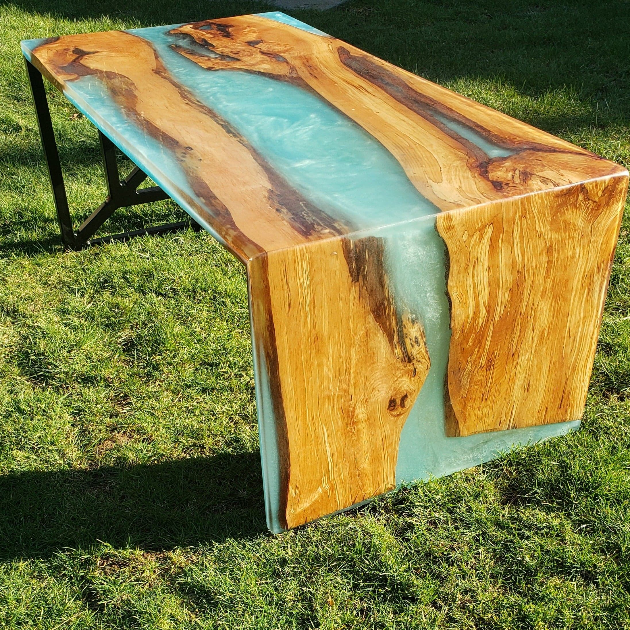 Live edge coffee table with a teal resin river running down the middle and over its waterfall end