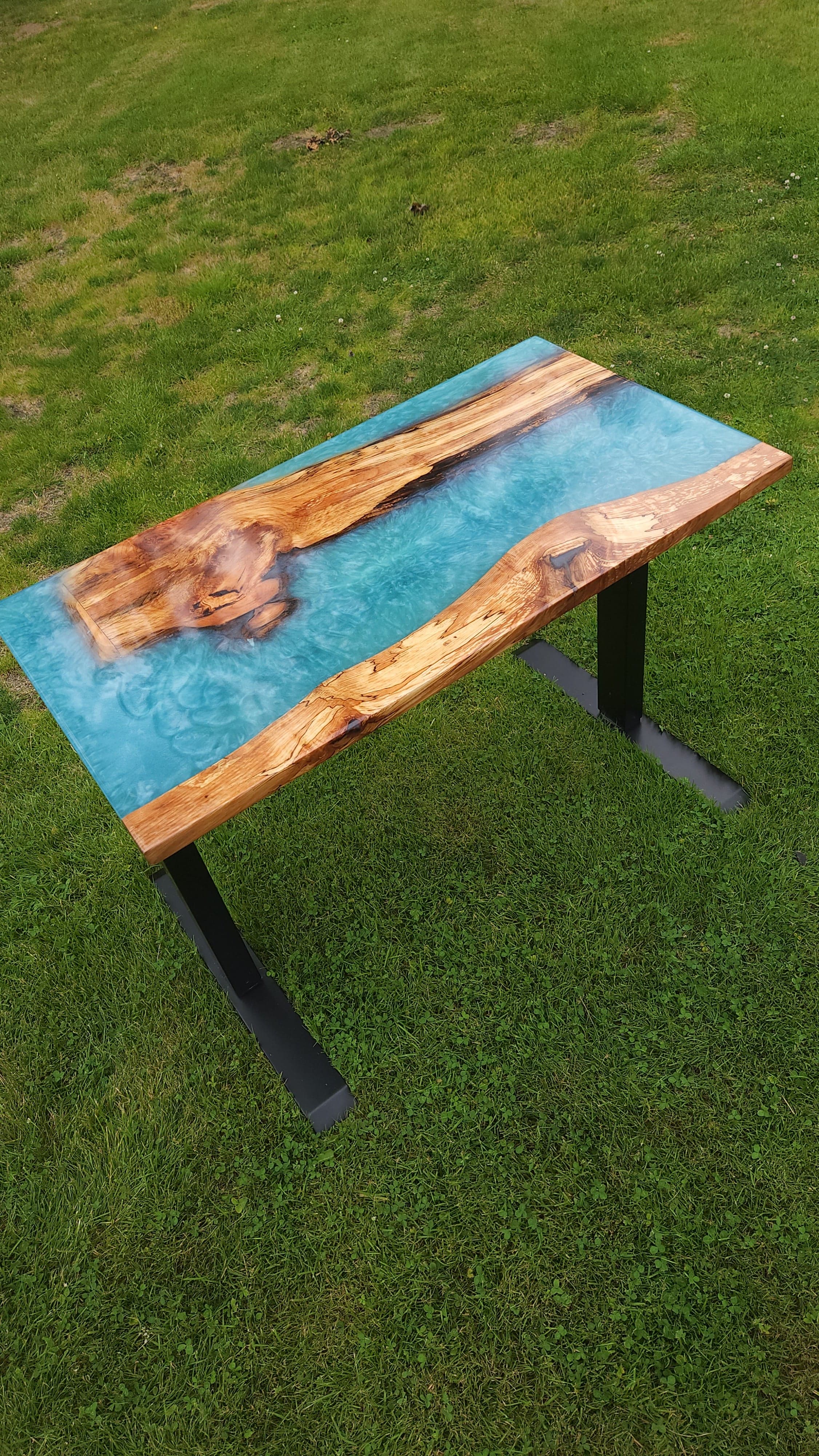 Live edge desk top with a pale teal resin river between two spalted edges, on black metal legs