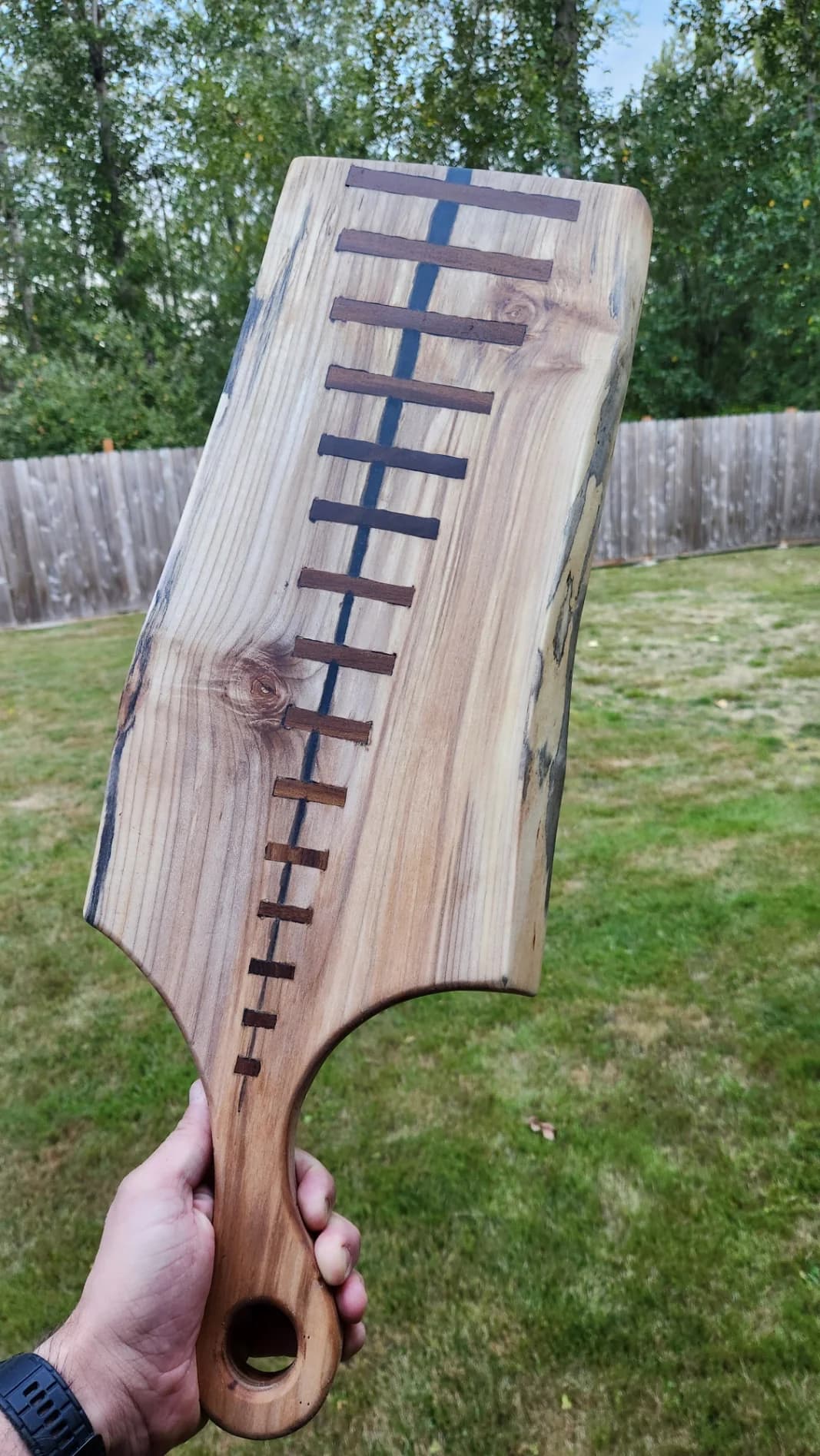 A hand holding a long live edge board inlaid with a row of dark wood stitches